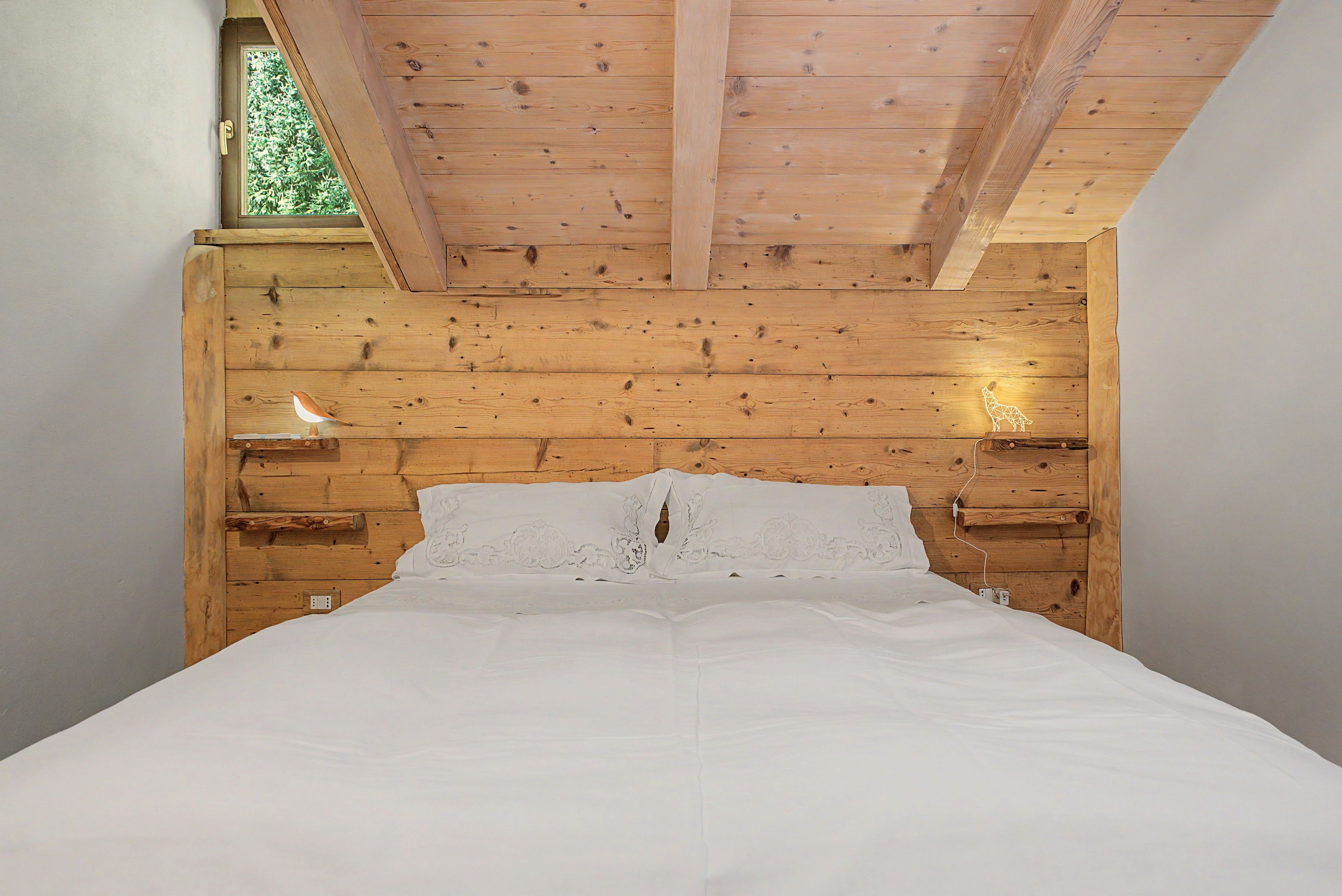Une chambre avec un plafond en bois, un lit avec une literie blanche et deux lampes fixées au mur.