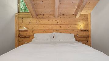Une chambre avec un plafond en bois, un lit avec une literie blanche et deux lampes fixées au mur.