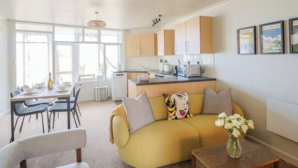 A modern kitchen with a dining area, a sofa with patterned cushions, and a vase with flowers. - 4 Kingfisher Court (Bridport)