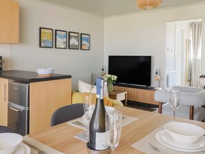 Cozinha moderna com área de refeições, televisão de tela plana e mesa posta com copos de vinho e garrafa.