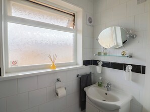 Une salle de bain avec une fenêtre, un miroir, un lavabo et un porte-serviettes.