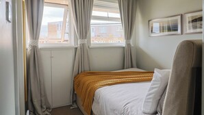 A bedroom with a bed, curtains, a window, and a wall-mounted light fixture. - 4 Kingfisher Court (Bridport)