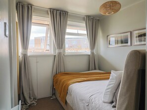Quarto com cama, cortinas, janela e luminária fixada na parede.