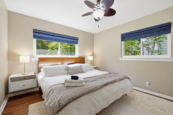 A bedroom with a bed, bedside tables, a ceiling fan, and windows with blue curtains.