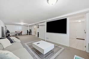 A modern living room with a white sofa, a coffee table, and a flat-screen TV mounted on the wall.