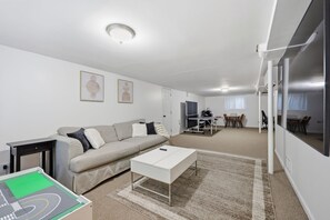 Een moderne woonkamer met een bank, salontafel en een tv-hoek met een tafel en stoelen.