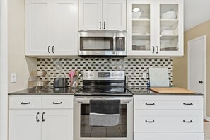 A kitchen with white cabinets, a stainless steel microwave, an oven, and a tiled backsplash. - Offering the perfect balance of quiet neighborhood living and urban convenience. (Durham)