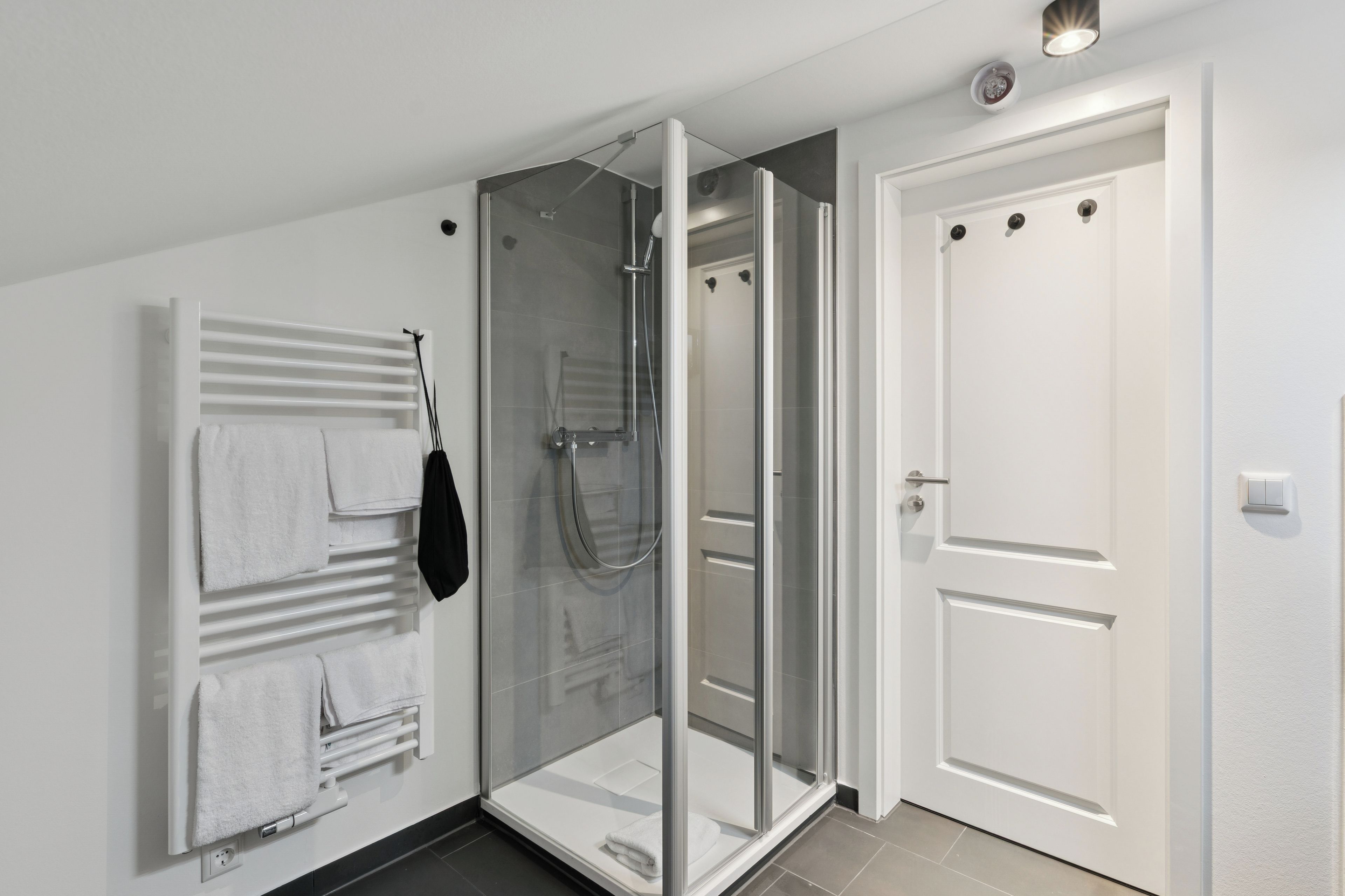 Un baño moderno con ducha envuelta en vidrio, un perchero con toallas dobladas y una puerta blanca.
