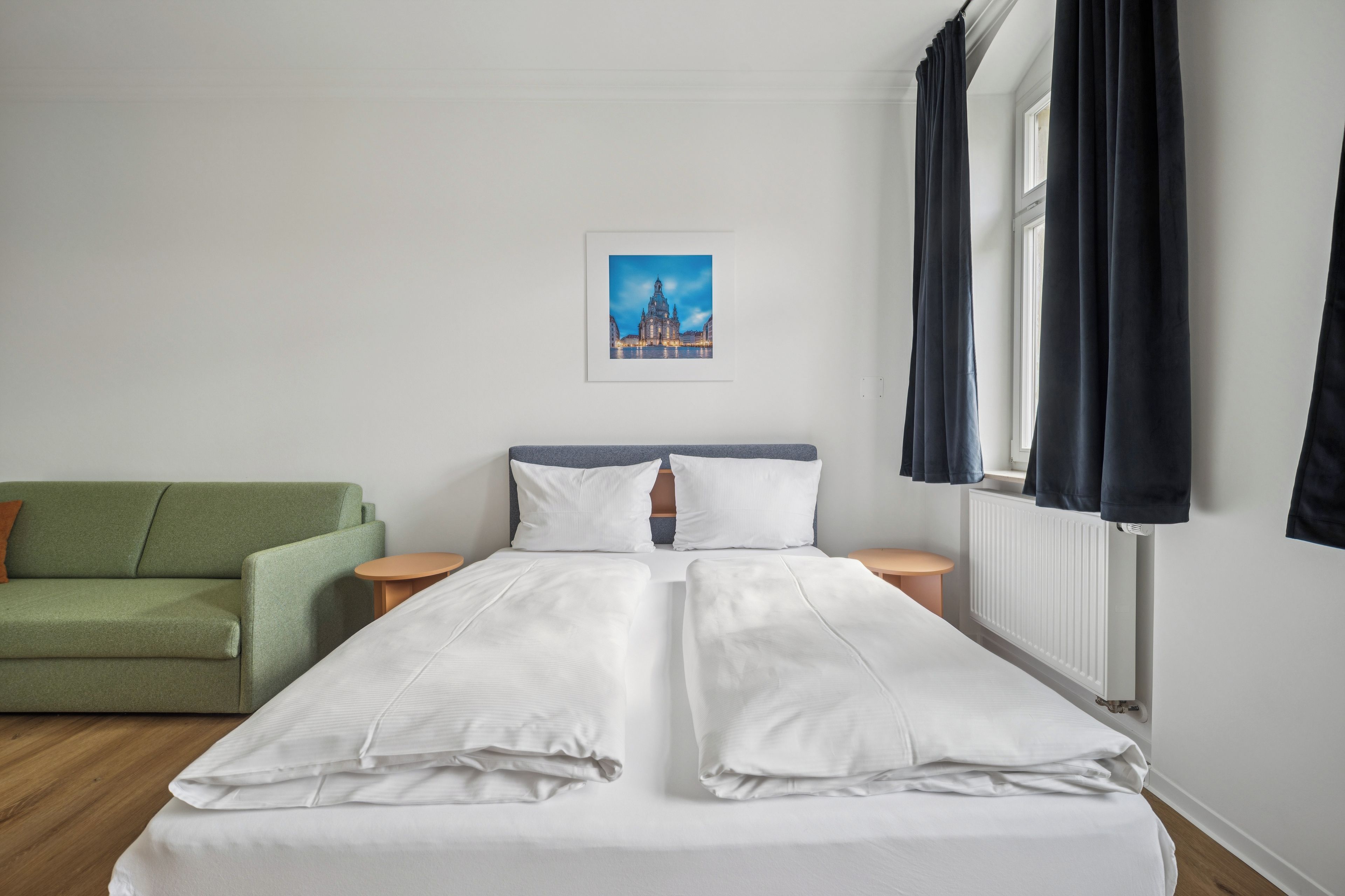 Una habitación de hotel con una cama, un sofá verde, una mesita y un cuadro en la pared.