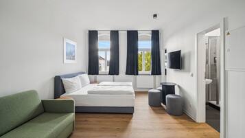 Ein modernes Schlafzimmer mit einem Bett, einem grünen Sofa, einem Fernseher und Blick ins Freie.