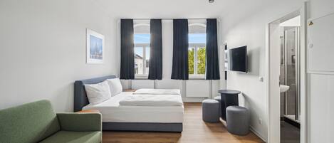 A modern bedroom with a bed, a green sofa, a TV, and a view of the outside.