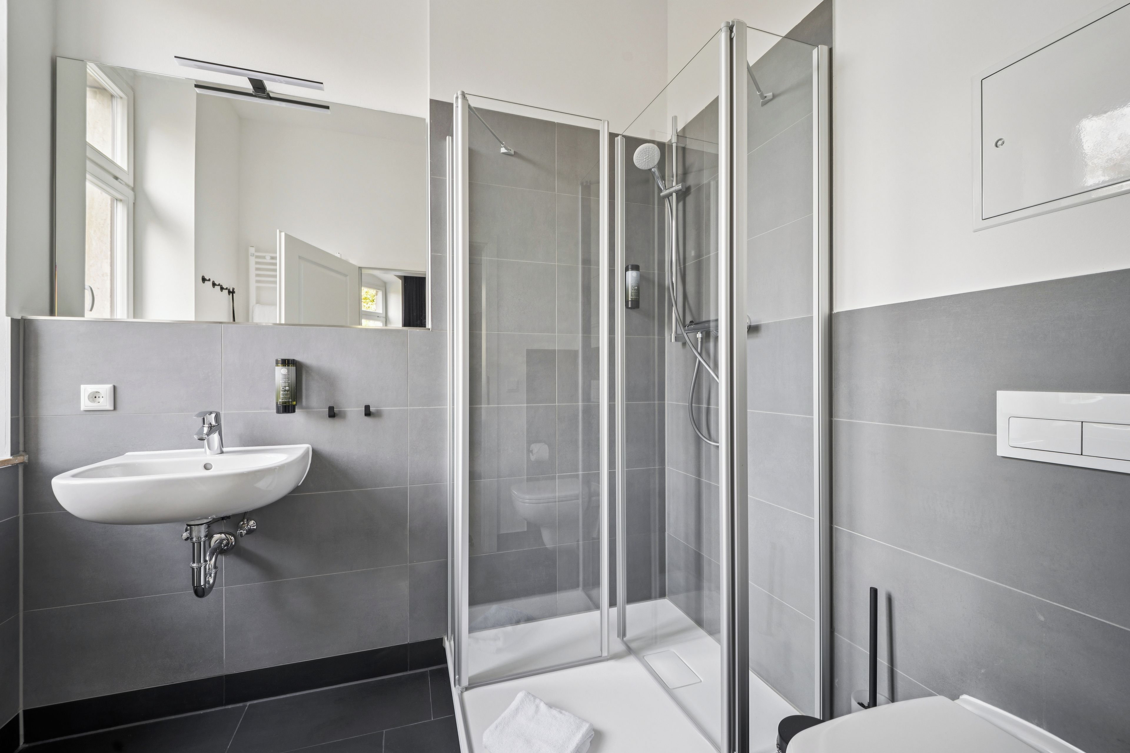 Ein modernes Badezimmer mit einer gläsernen Dusche, einem weißen Waschbecken und einem Spiegel.