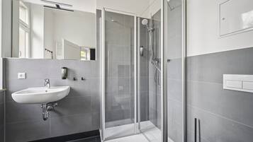 Ein modernes Badezimmer mit einer gläsernen Dusche, einem weißen Waschbecken und einem Spiegel.