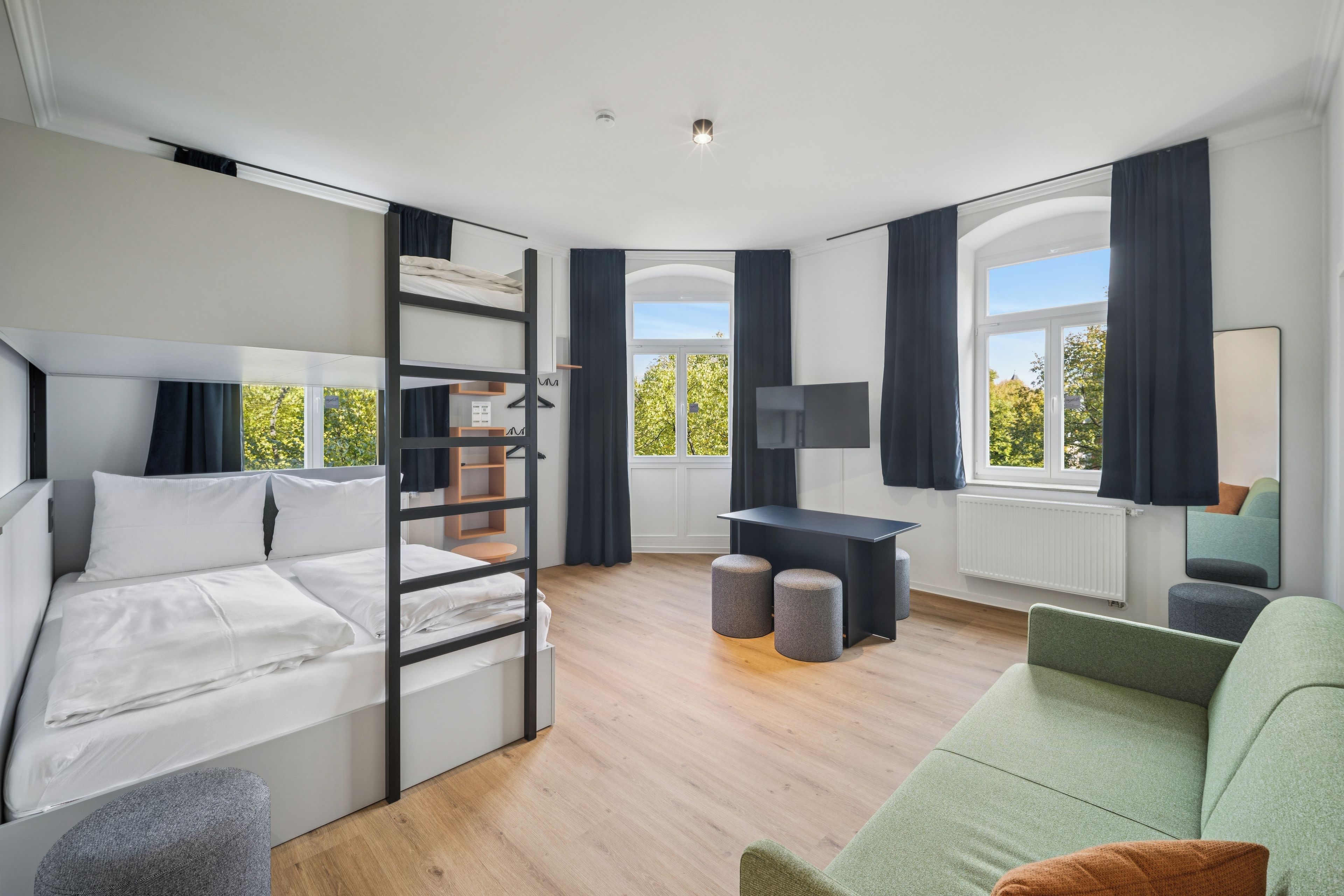 Ein modernes Schlafzimmer mit Etagenbett, Schreibtisch, Sofa und großen Fenstern.