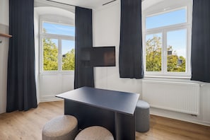 Una habitación moderna con televisión de pantalla plana en la pared, una mesa oscura y dos otomanas redondas.