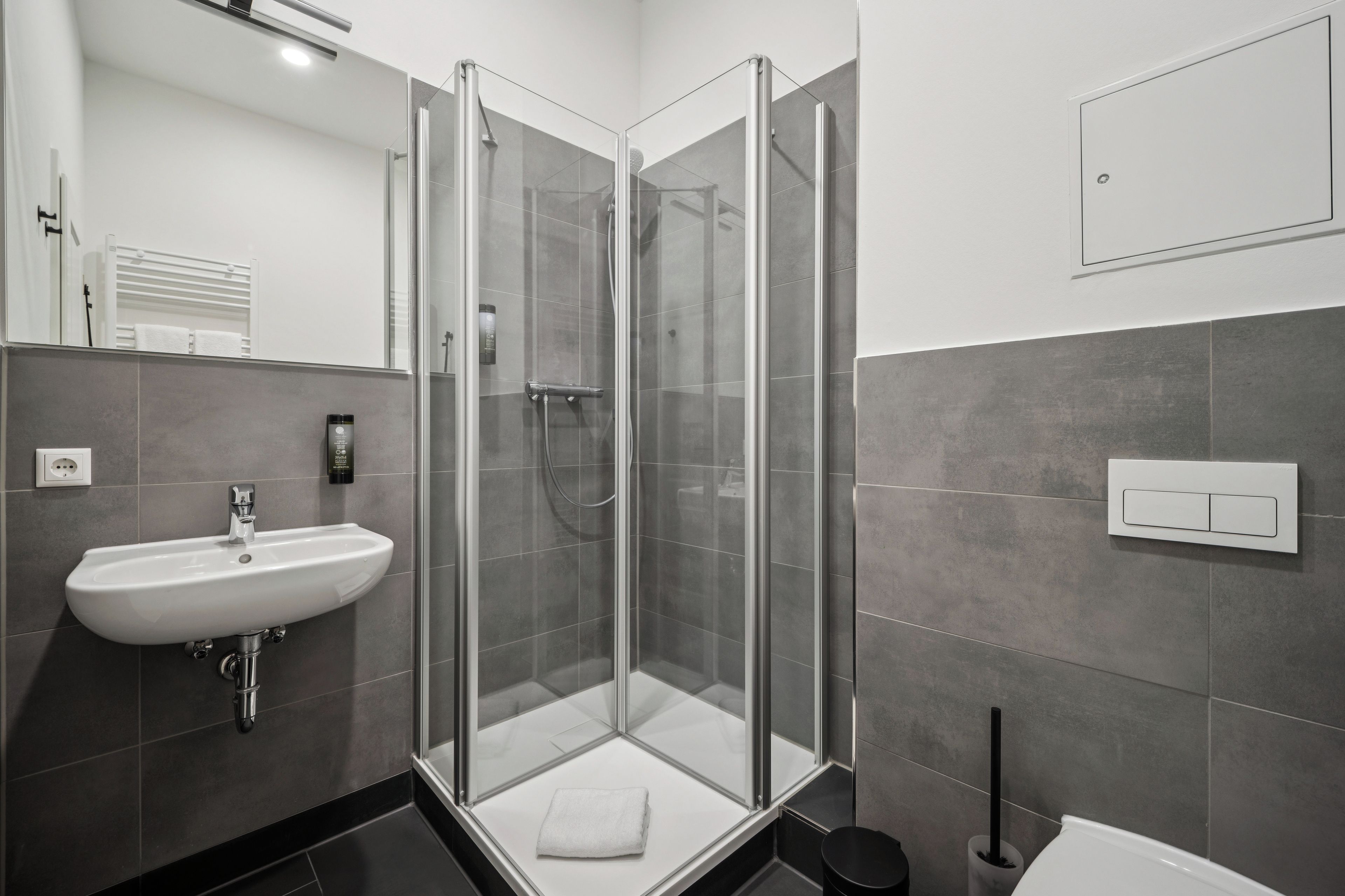 Un baño moderno con ducha envuelta en vidrio, un lavamanos blanco y una toalla en el suelo.