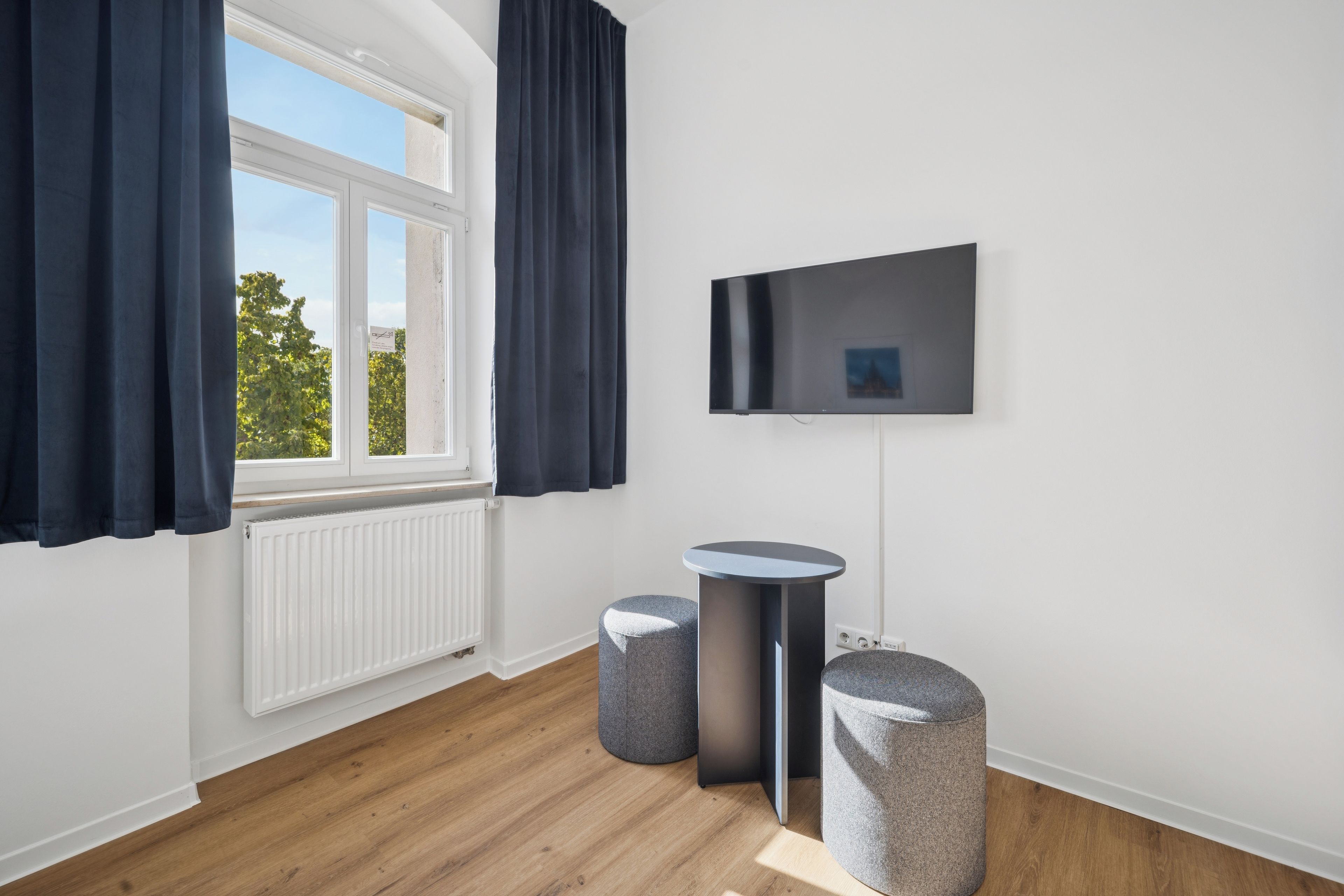 Ein modernes Zimmer mit großem Fenster, einem an der Wand befestigten Flachbildfernseher und zwei runden Hocker.