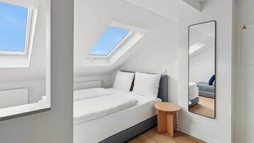 A modern bedroom with a skylight, a bed, a round wooden table, and a large mirror.