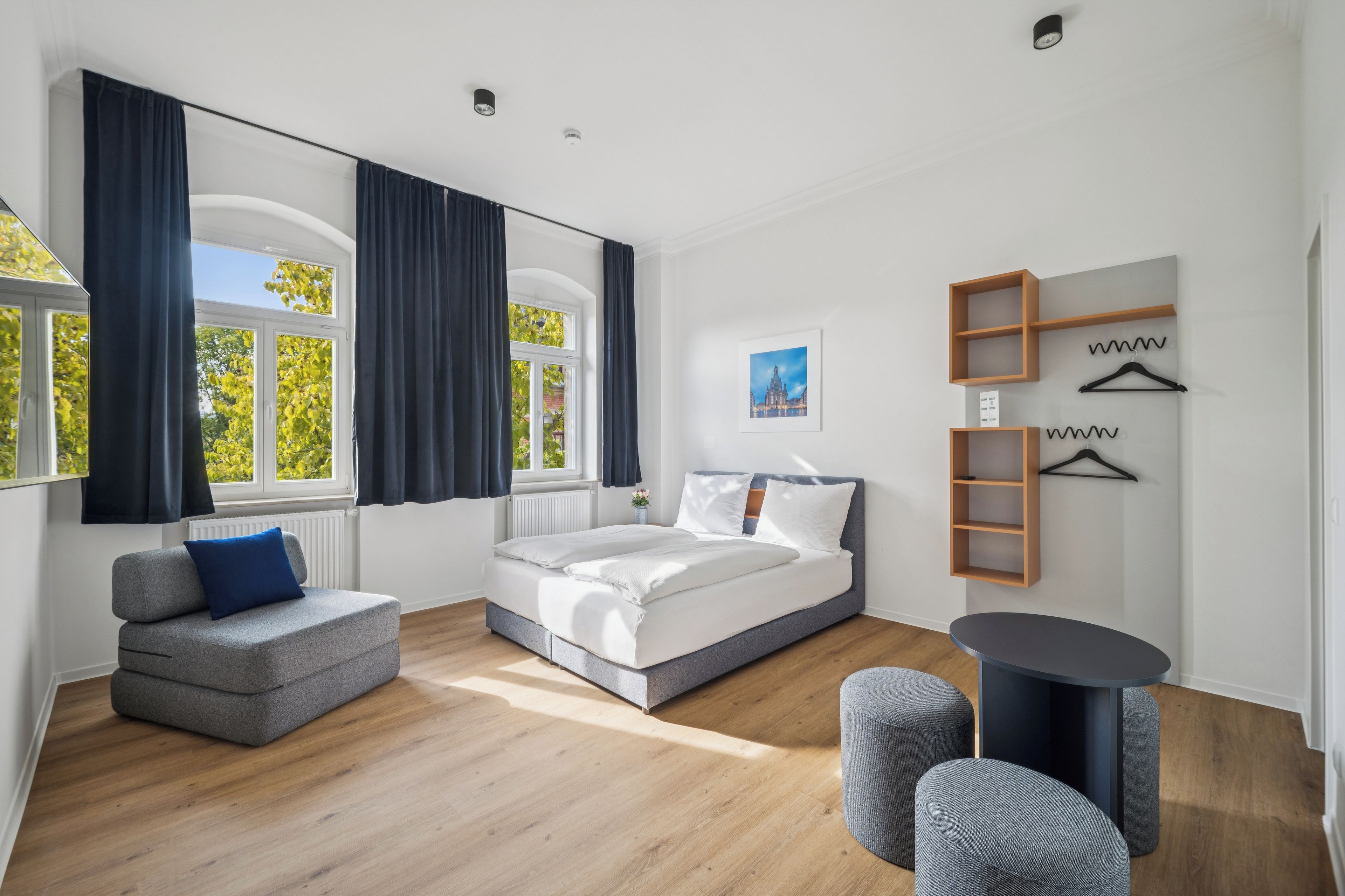 Ein modernes Schlafzimmer mit Bett, Sofa, rundem Tisch und Spiegel.