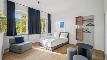 Ein modernes Schlafzimmer mit Bett, Sofa, rundem Tisch und Spiegel.
