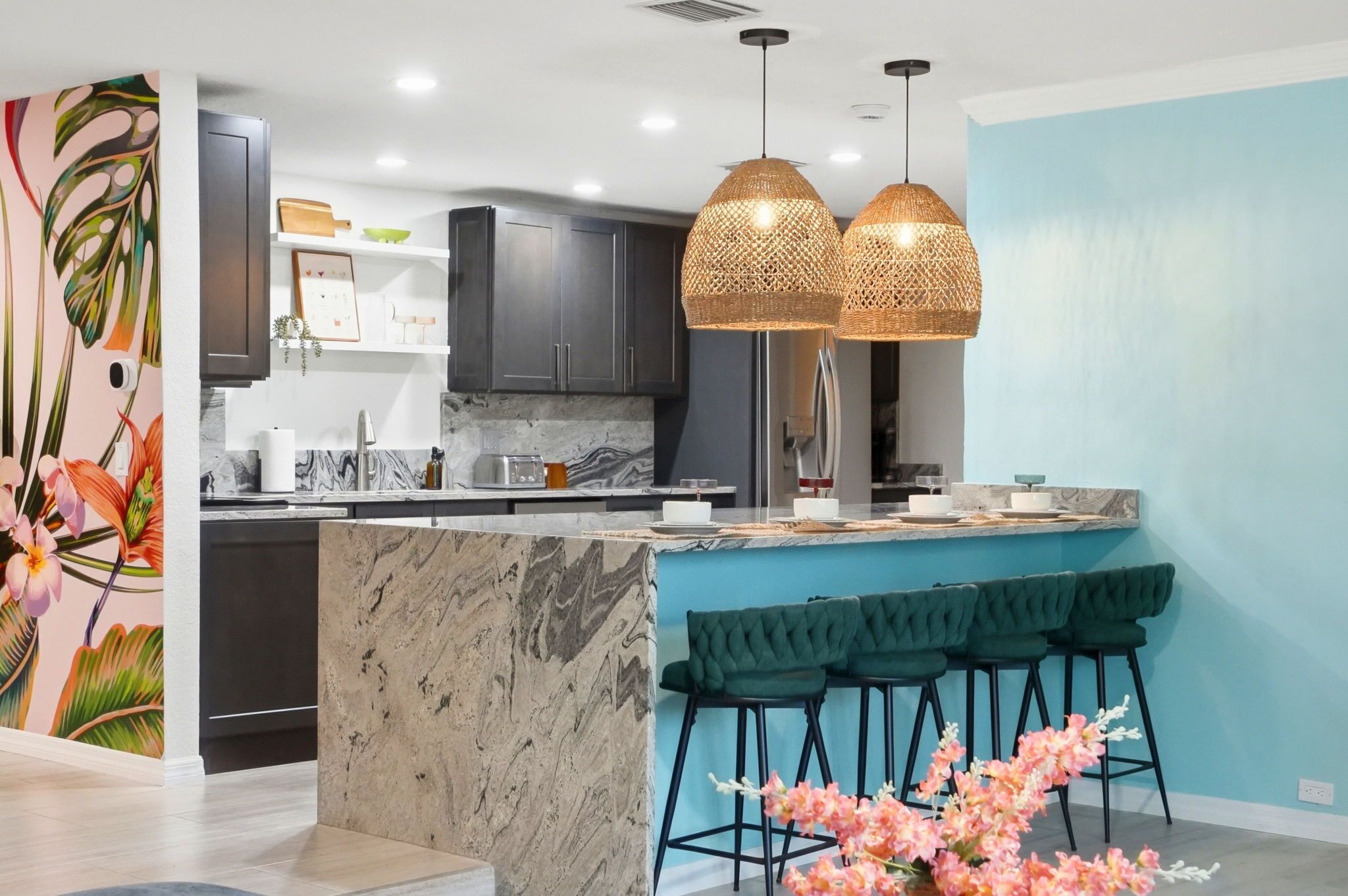A modern kitchen with dark cabinets, a marble island, and a teal accent wall.