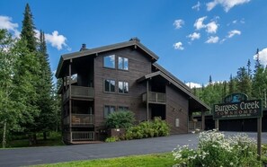 Ein zweistöckiges Gebäude mit Balkon, umgeben von Bäumen und blauem Himmel.