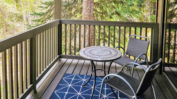 A covered outdoor area with a table and chairs, surrounded by a railing, overlooking a forested area. - Spacious updated 2-bedroom townhome in Steamboat Springs perfect for getaway (Steamboat Springs)
