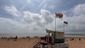 A lifeguard station on a beach with a flag, a lifeguard booth, and people in the background.