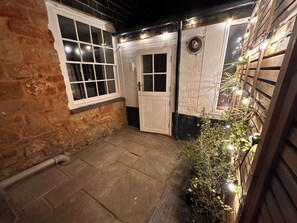 A stone wall, a white door, and a small garden area with plants and lights.