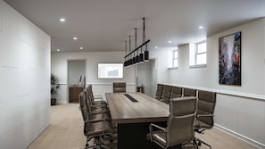 A conference room with a long table, multiple chairs, a projector screen, and a painting on the wall.