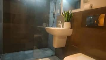 A modern bathroom with a glass-enclosed shower, a white sink, a toilet, and a small potted plant.