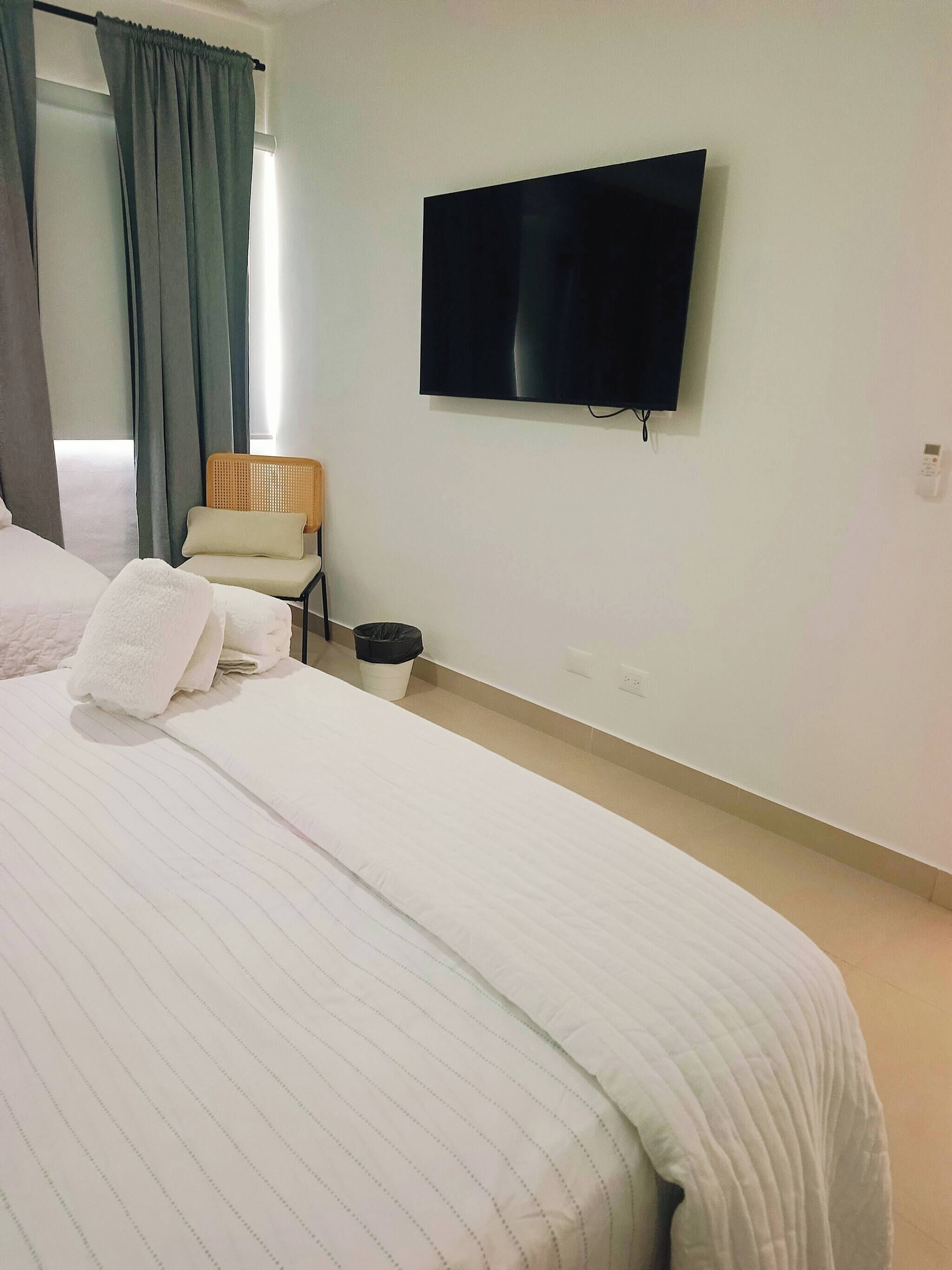 Une chambre d’hôtel avec un lit, un téléviseur fixé au mur, une chaise et une poubelle.