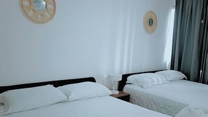 Een hotelkamer met twee bedden, witte lakens, een nachtkastje met een lamp en een decoratie aan de muur.