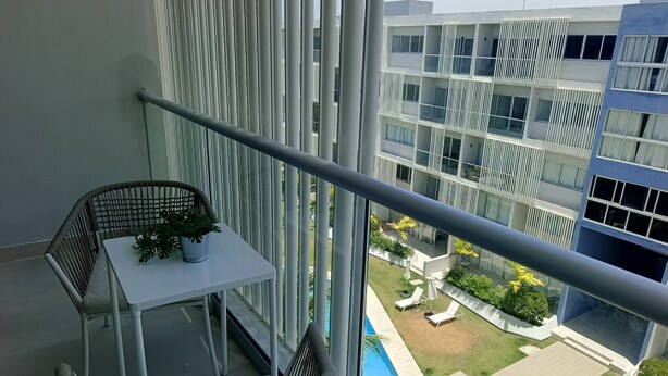 Een balkon met een tafel en stoelen, met uitzicht op een zwembad en een aangelegde tuin met ligbedden.
