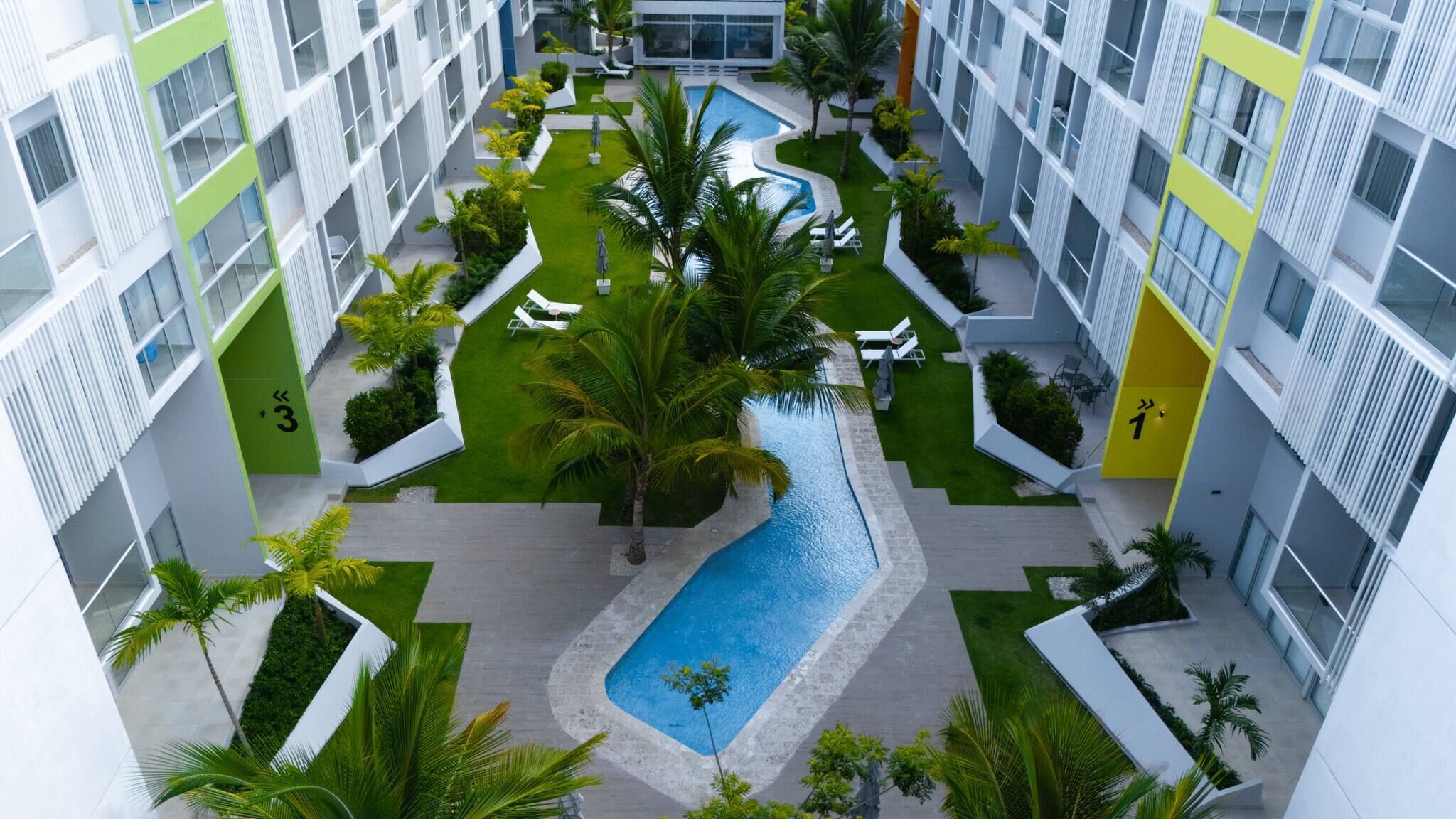 A modern building with a central pool, surrounded by greenery and numbered balconies.