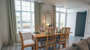 A dining area with a table set for four, wooden chairs, and a view of the outdoors through large windows. - Beach Court by Guestz (Trearddur Bay)