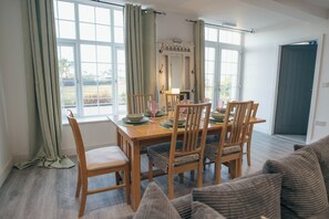 Ein Essbereich mit einem Tisch für vier Personen, Holzsesseln und Blick ins Freie durch große Fenster.