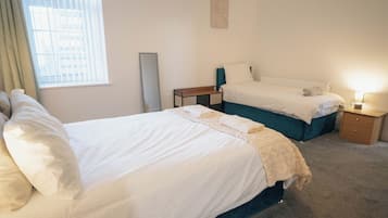 A hotel room with two beds, a bedside table, a lamp, and a window with blinds.