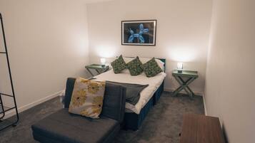 A bedroom with a bed, two bedside tables, a nightstand, a chair, and a picture on the wall.