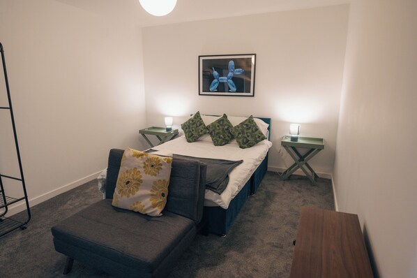 A bedroom with a bed, two bedside tables, a nightstand, a chair, and a picture on the wall.