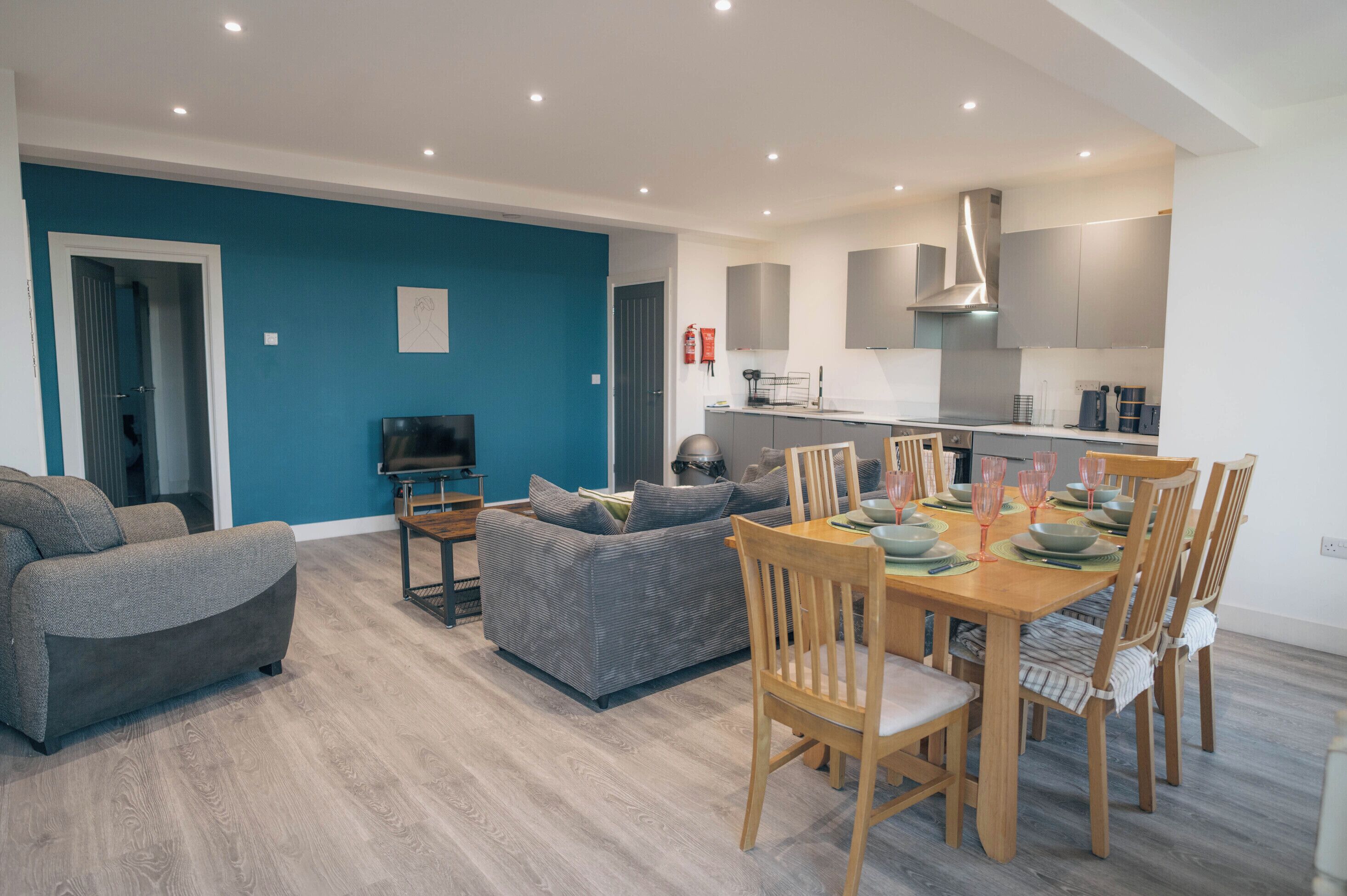 A modern living room with a sofa, a dining table set for four, and a kitchen in the background.