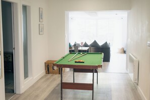 A pool table in a room with a wooden floor, a door on the left, and a window on the right.