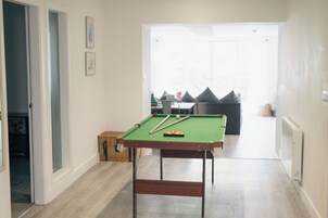 Una mesa de billar en una habitación con piso de madera, una puerta a la izquierda y una ventana a la derecha.