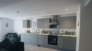 A modern kitchen with grey cabinets, a built-in oven, and a countertop with various appliances. - Beach Court by Guestz (Trearddur Bay)