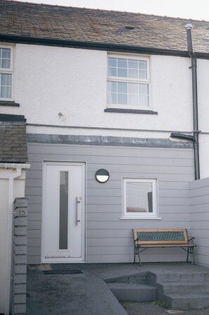 A residential building with a white exterior, a front door, a small window, and a bench.