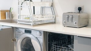 A compact laundry area with a front-loading washing machine, a built-in drying rack, and a toaster on the countertop. - Beach Court by Guestz (Trearddur Bay)