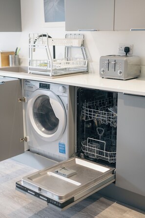 Ein kleiner Waschbereich mit einer Frontlader-Waschmaschine, einem eingebauten Wäscheständer und einem Toaster auf der Arbeitsplatte.