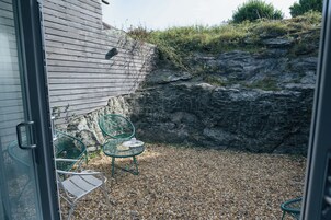 A patio with two green chairs and a table, gravel ground, and a wooden wall.