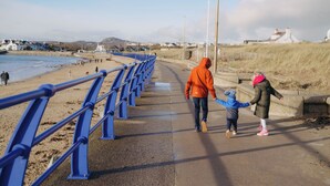 A coastal walkway with a blue railing, a beach, and houses in the background. - Beach Court by Guestz (Trearddur Bay)