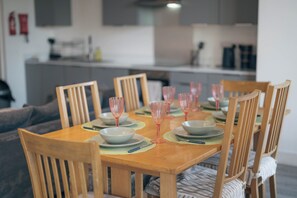 Une table à manger dressée avec des assiettes, des bols et des verres à vin roses, entourée de chaises en bois.